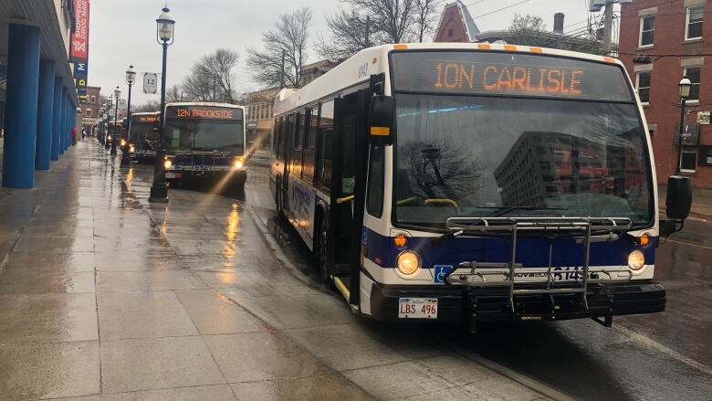 A rainy sidewalk with city buses parked next to it