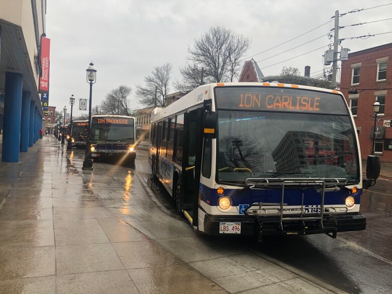 A rainy sidewalk with city buses parked next to it