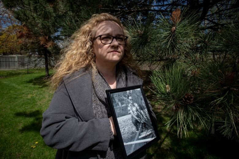 A woman holding a framed photograph of a man looks away from the camera for a photo.