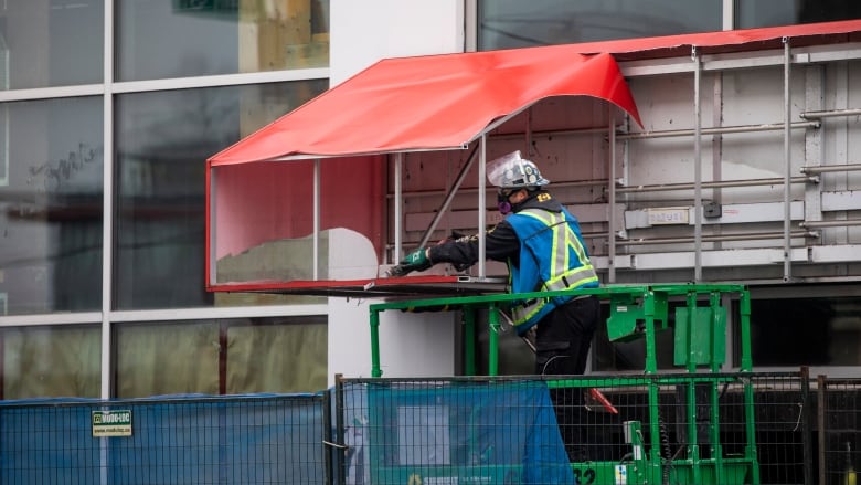 A construction worker in a high-visibility vest uses a drill.