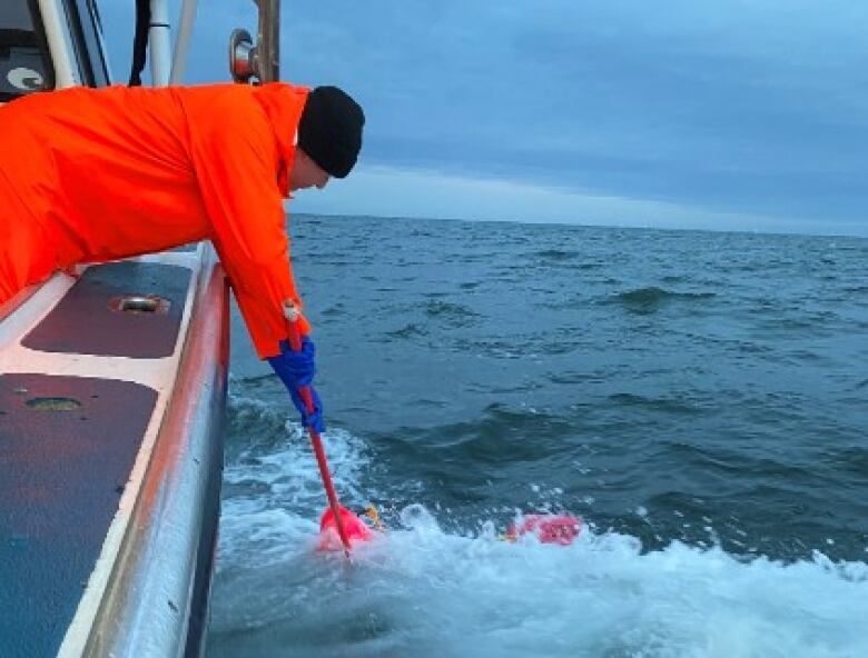 A fisherman in a red outfit leans over the side of a boat.