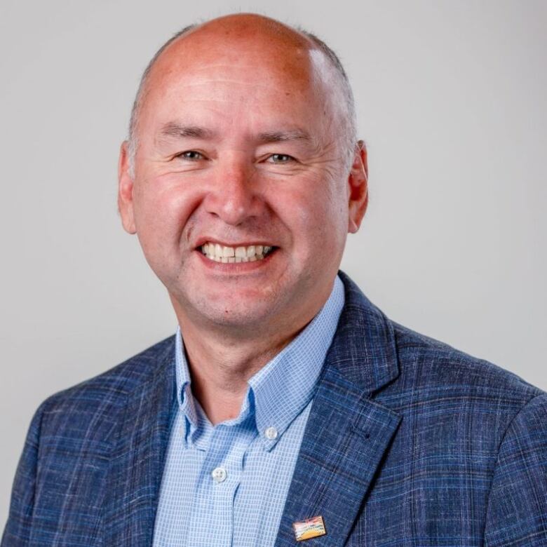 A bald-headed man in a blue suit smiles for the camera.