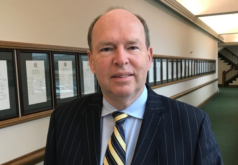 A smiling man wears a blue suit with a yellow striped tie.