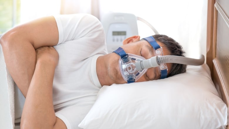 Man sleeping in bed on his side hooked up to a CPAP machine.