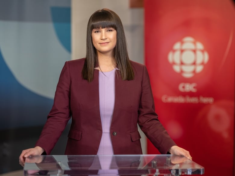 Meghan Roberts stands at her CBC North news desk. She wears a burgundy blazer with a pick blouse underneath. 