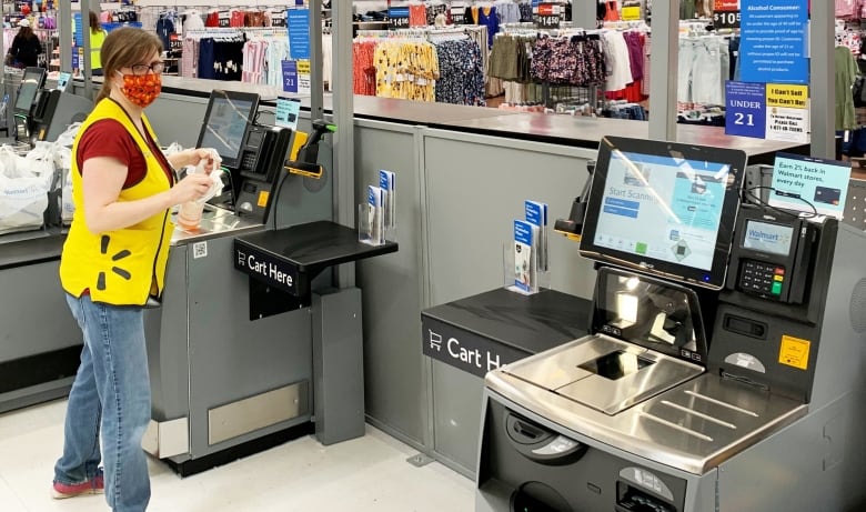 A Walmart self-checkout attendant stands in front of several machines in the store. 