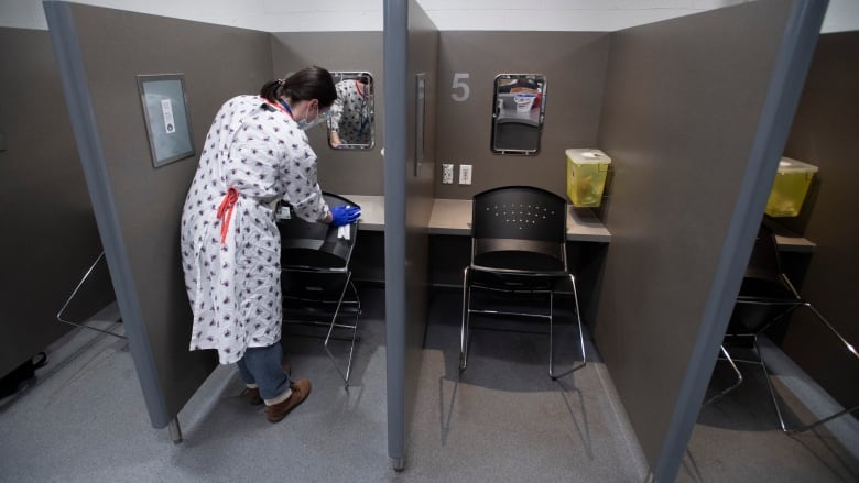 A woman in a white gown cleans the backside of a chair, located in a narrow booth.