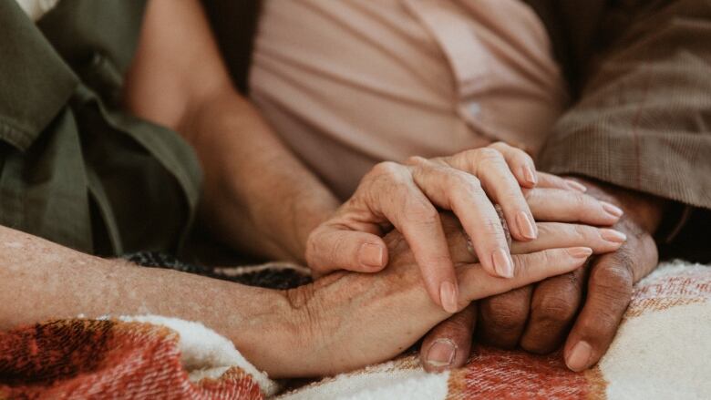 A closeup shows the hands of a senior person resting gently on the hands of another senior.