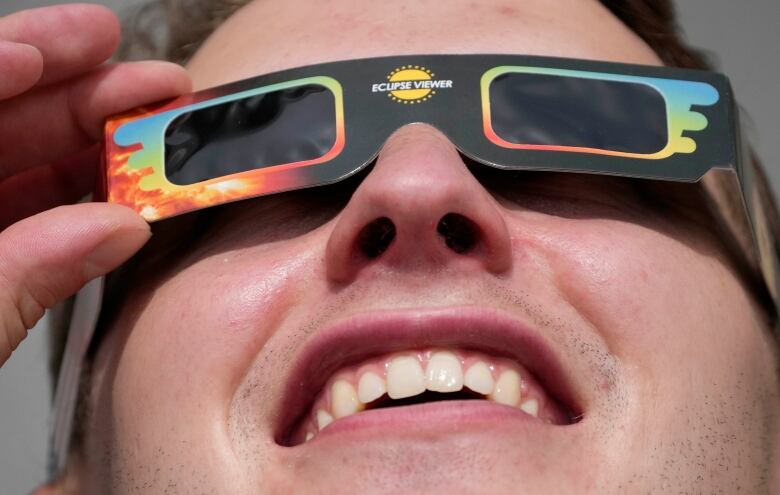 Closeup of man wearing cardboard and plastic glasses with the words eclipse viewer in the middle.