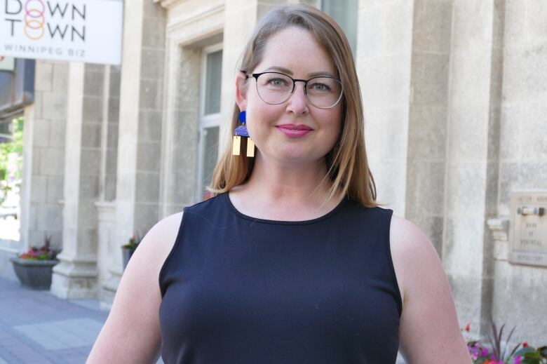 A woman wearing glasses stands outside a building.