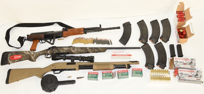 A while table is covered in guns and ammunition.