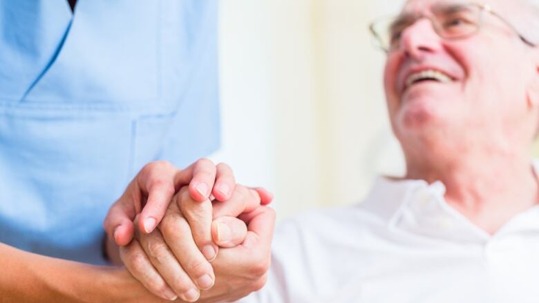 A nurse holds the hand of a senior man wearing glasses.