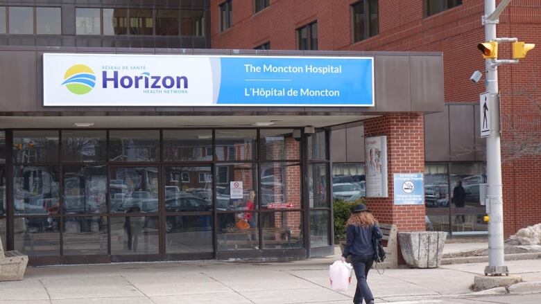 The front entrance of a brick building has a row of glass doors across the front and a sign above that says in blue and white letters Horizon The Moncton Hospital.