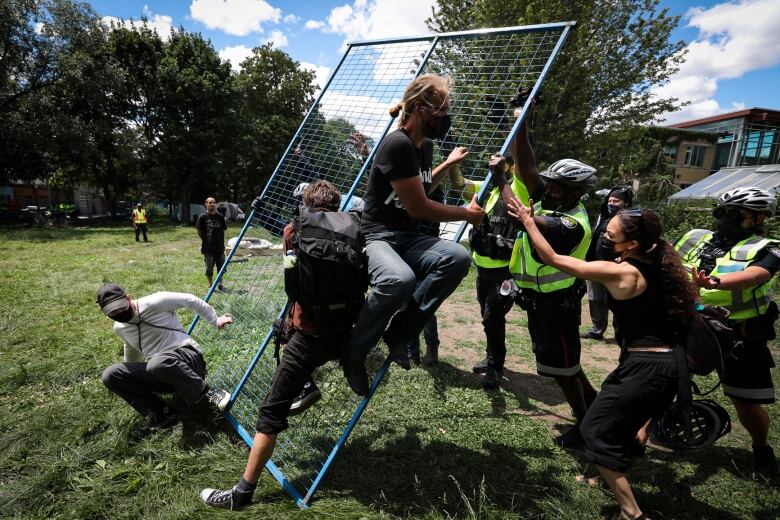 Supporters try to take down a fence as occupants of a homeless encampment at Toronto's Trinity Bellwoods Park await their possible eviction by police after workers enclosed the area with a fence on Tuesday.