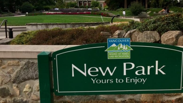 A sign that reads 'New Park Yours to Enjoy', in the foreground of a large park.