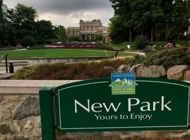 A sign that reads 'New Park Yours to Enjoy', in the foreground of a large park.