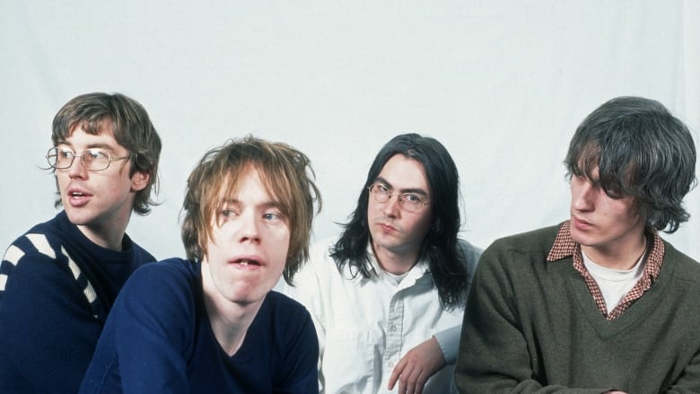 Four people in a row pose for the camera in front of a white backdrop.