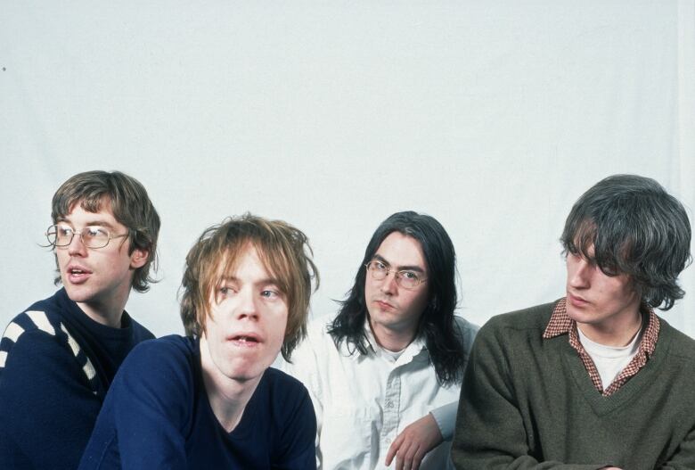 Four people in a row pose for the camera in front of a white backdrop.