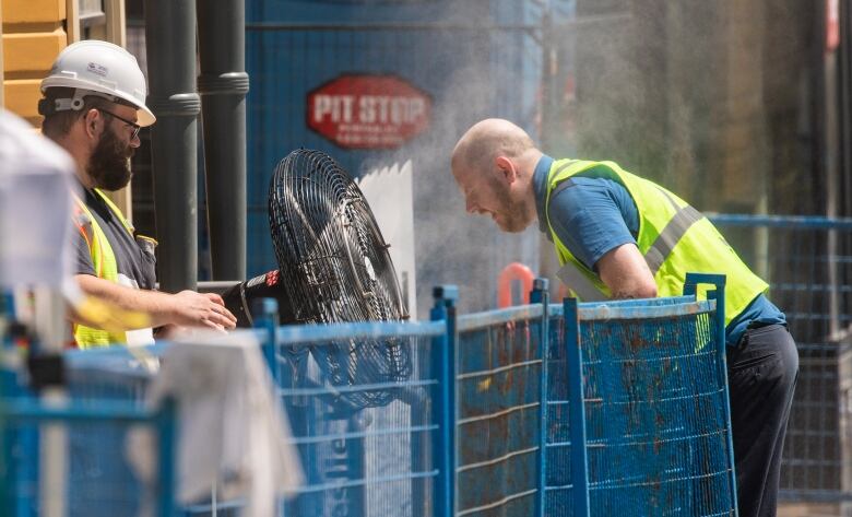 A construction worker uses a misting fan during a heat wave.