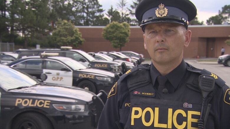 A police officer in uniform stands in a parking lot filled with police vehicles.