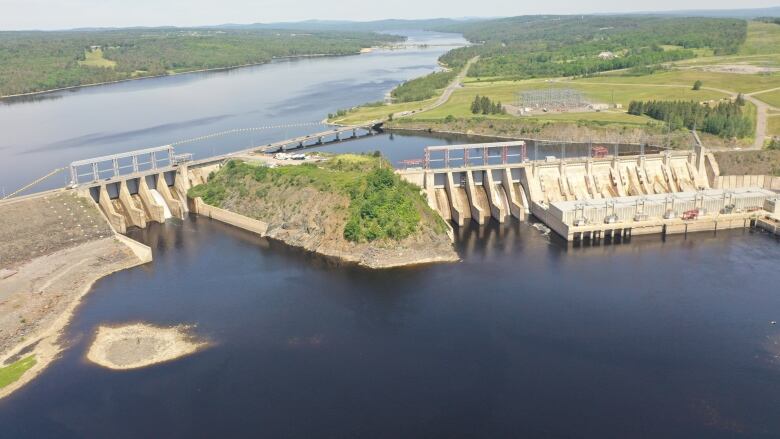 An aerial shot of a dam surrounded by water with green grass and trees on the banks.