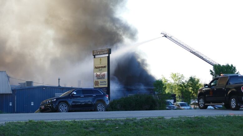 Fire crews using an aerial ladder douse a fire from above. Heavy smoke is coming up.