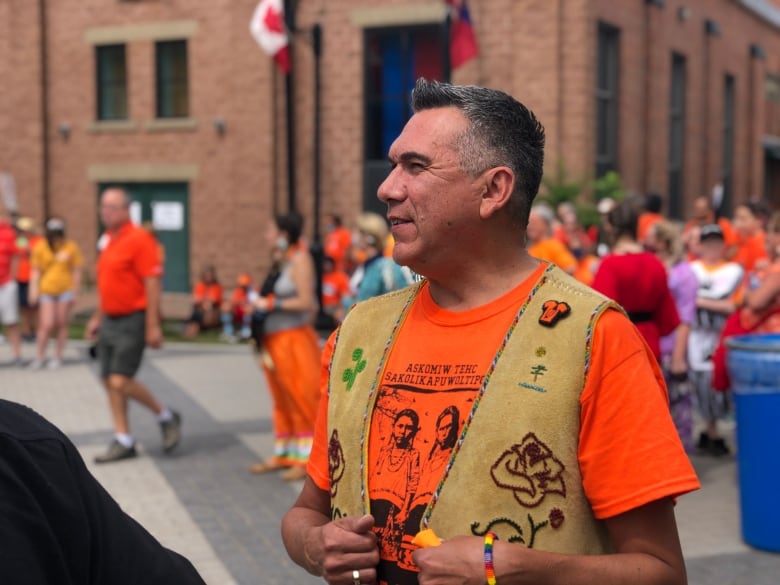 A man stands up outside wearing an orange shirt.