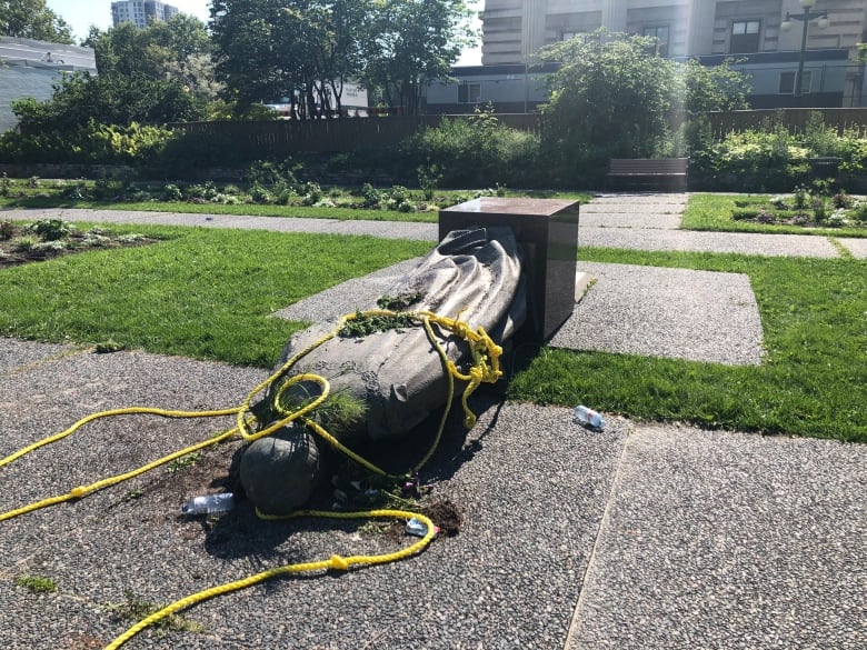 A statue lies face down with yellow ropes tied around it.