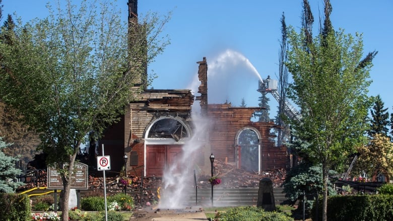 Man on a crane uses fire hose on brick church.