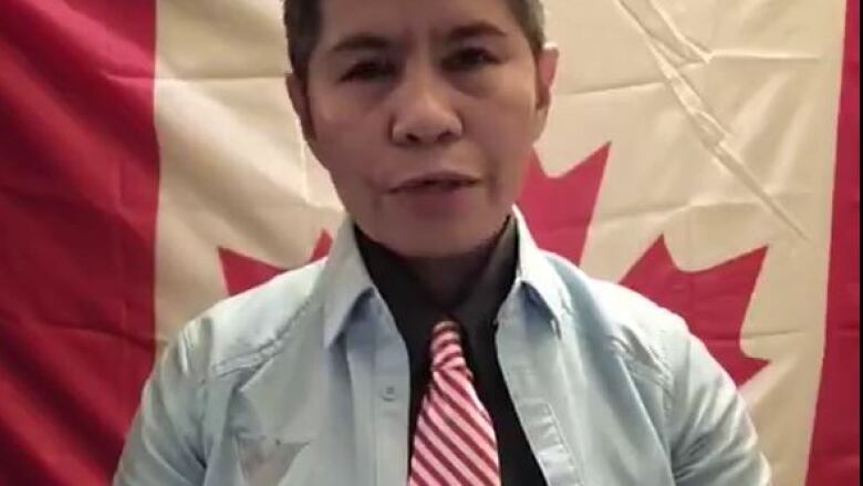 An Asian woman wearing a shirt and red-and-white striped tie is in front of a Canada flag.