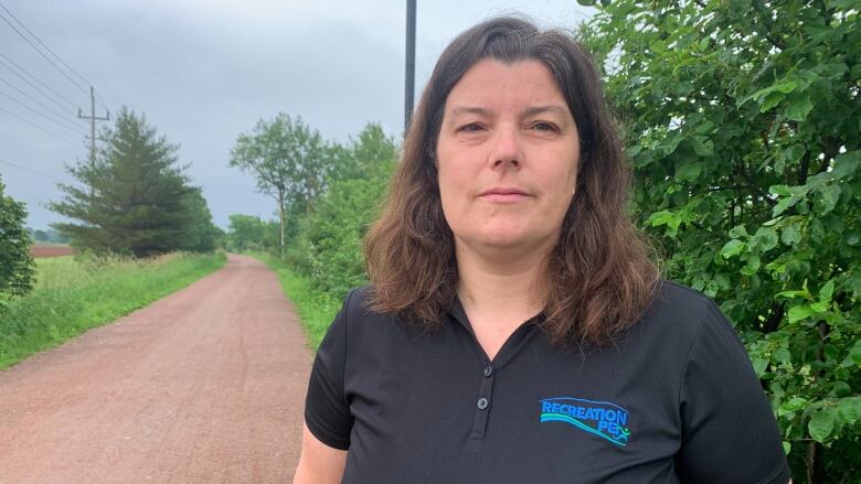 Woman in a navy blue shirt stands in front of a trail. 