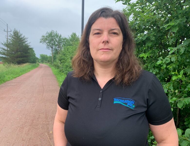 Woman in a navy blue shirt stands in front of a trail. 