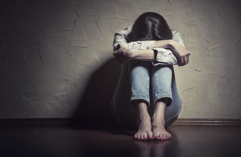 A young sad woman sitting alone on the floor in an empty room. Her head is buried in her knees.