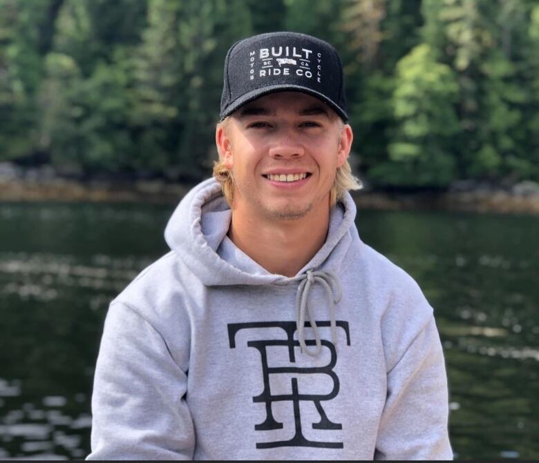 A photo of a smiling young man in a black ball cap and grey hoodie.