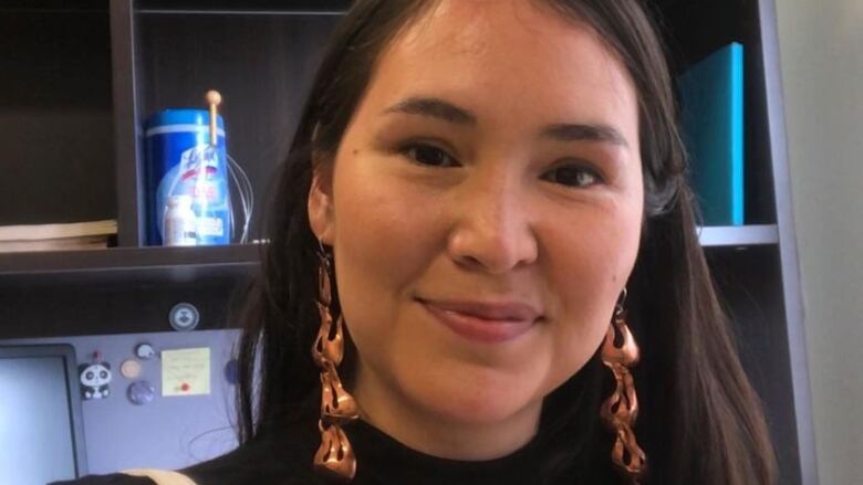 A young woman with long dark hair and earrings is seen in a close up photo 