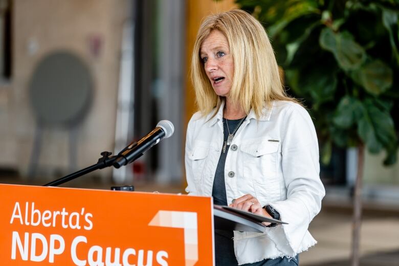 A woman making a speech stands at a podium with an orange placard in the front.