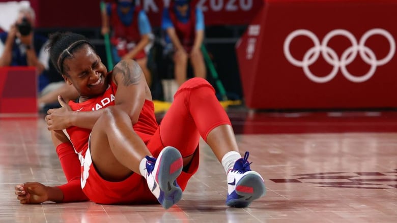 A Black woman on a basketball court laying on the ground and clutching her shoulder