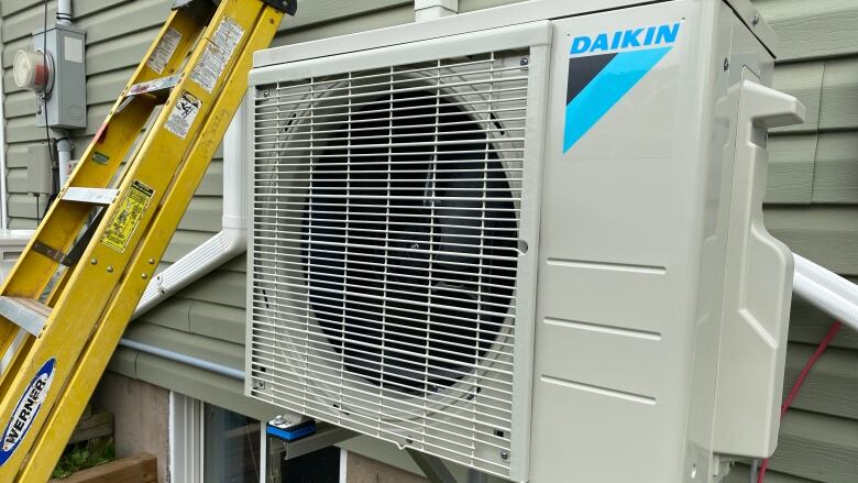 A heat pump on the outside of a house with a yellow ladder next to it