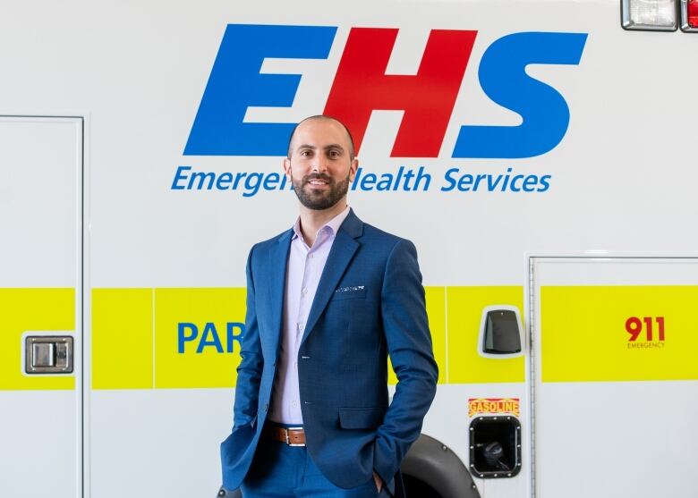 A man in a blue suit stands in front of an ambulance.