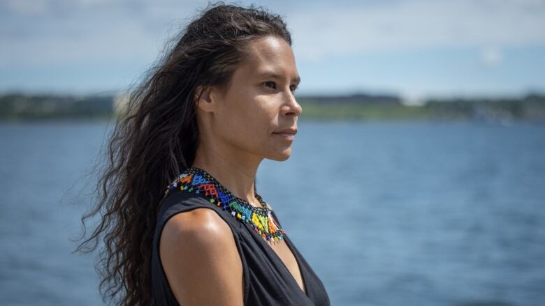 A woman with long dark hair is wearing a beaded necklace and a black tank top