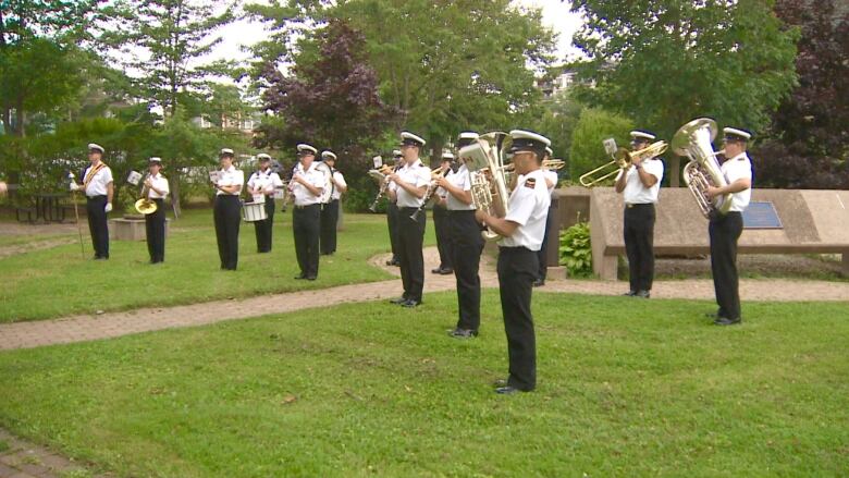 A group of people wearing professional army clothing are playing wind instruments on a lawn