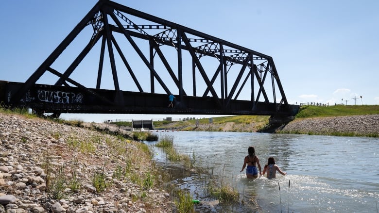 2 teens swim in a river near a bridge. 