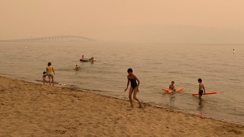 Children play on the Hot Sands Beach in downtown Kelowna, B.C., near the Okanagan Lake with low visibility of William R. Bennett Bridge amid heavy wildfire smoke on July 30, 2021.