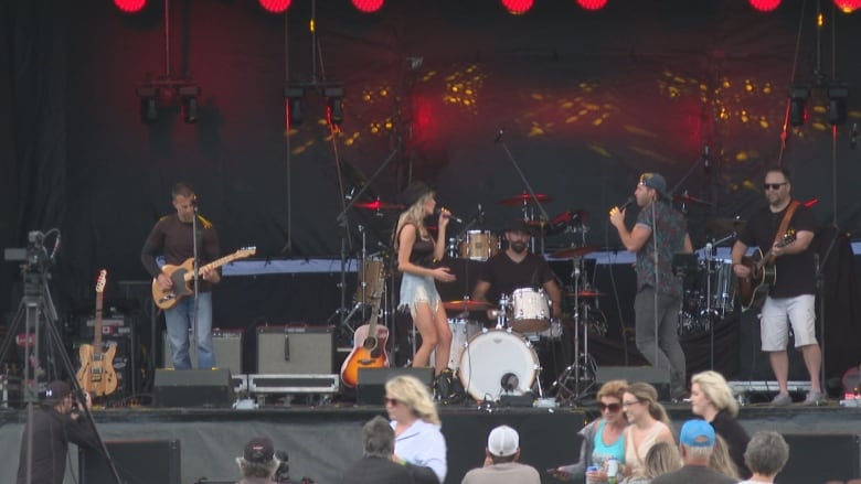 A woman sings on stage with musicians around her and red lights in the background. 