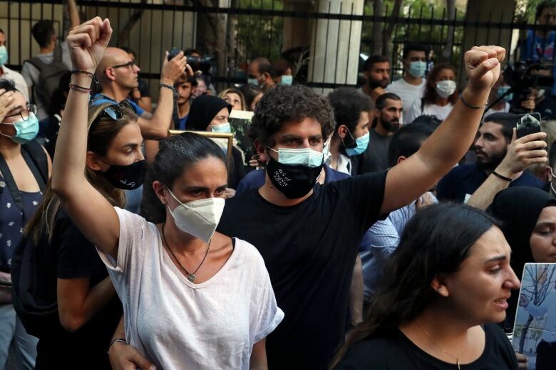 A man and a woman standing in a crowd, both wearing masks and holding their fists in the air. The man has his arm around the woman's waist.