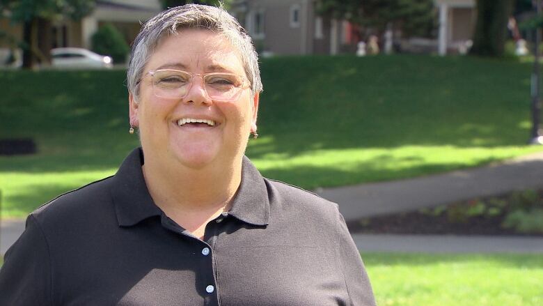 A woman with short grey hair and glasses wearing a black shirt smiles.