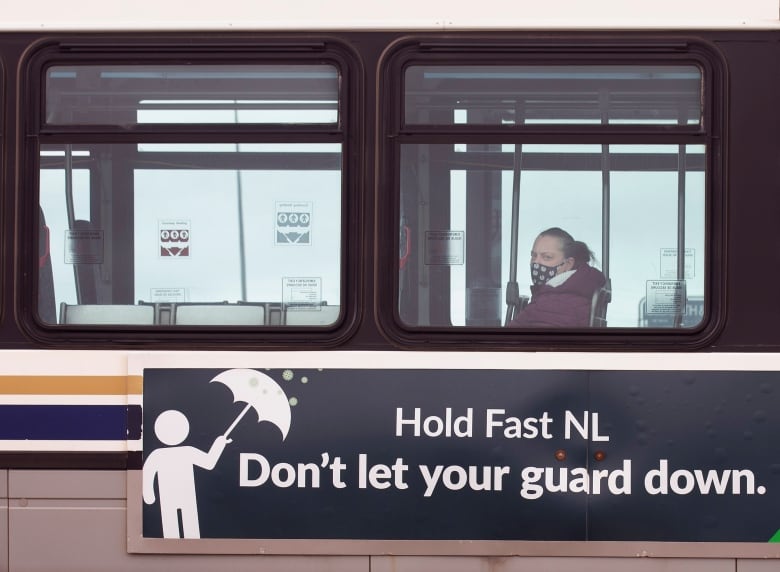 A lone woman sits in a bus, which has an ad on the side reading Hold Fast N.L., Don't let your guard down.