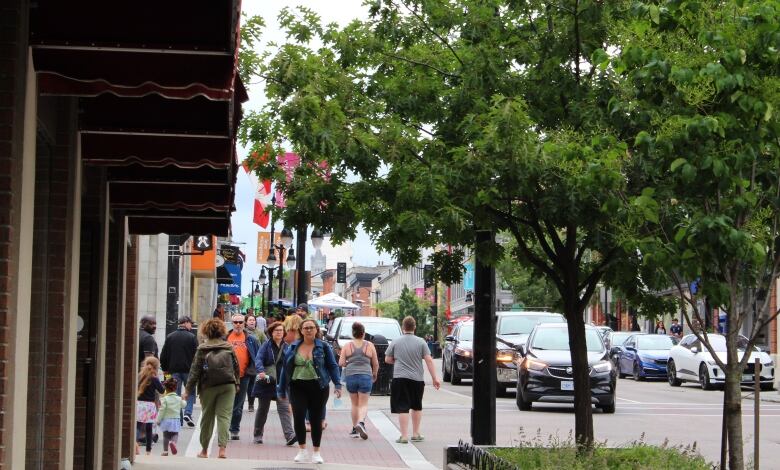 A downtown street in the summer with several pedestrians walking along the sidewalk.