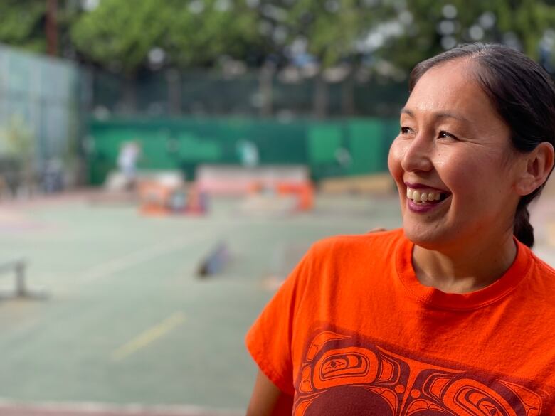 A woman in an orange shirt smiles at a skate park.