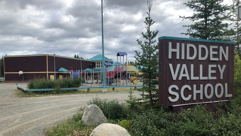 A school building is seen from the outside, with a sign reading 'Hidden Valley School.'